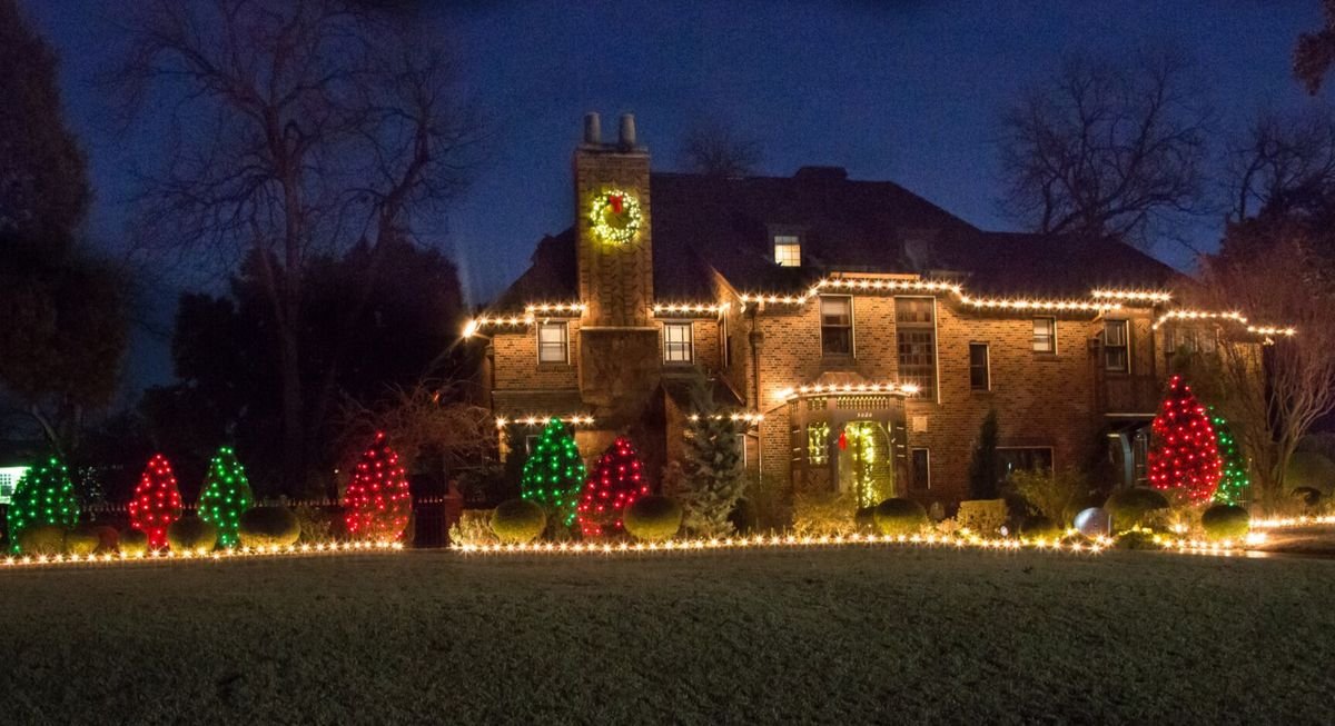 Home with warm white roofline lighting and red and green wreaths on trees