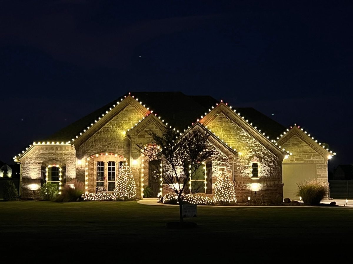 Home with warm white roofline lighting and lit trees in the front yard